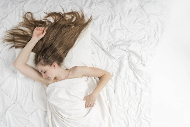 Mooie jonge vrouw slaapt in haar bed op witte lakens thuis. Bovenaanzicht portret van slapend meisje met lang los haar. Kopieerruimte. - Foto, afbeelding