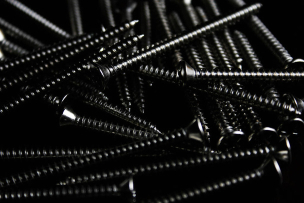 The screws are placed on a black wooden table with lighting from the side in thailand. - Фото, зображення