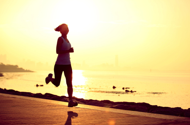 Juokseva urheilija juoksee meren rannalla. nainen kunto siluetti auringonnousu lenkkeily workout hyvinvointi käsite
. - Valokuva, kuva