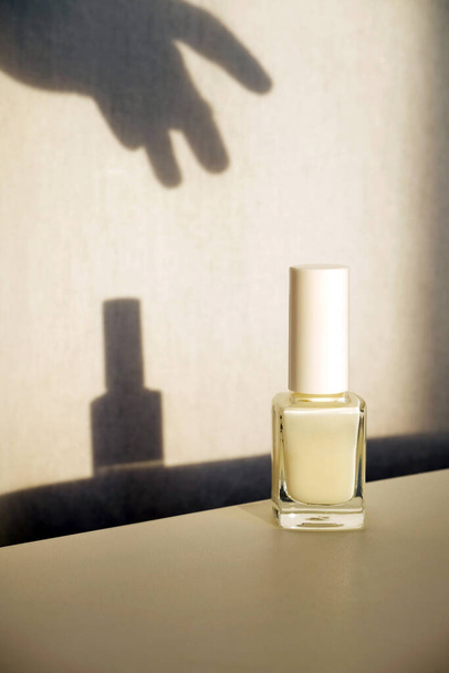 Esmalte de uñas blanco o producto de cuidado de uñas en botella de vidrio. Sombra de alcanzar la mano. Concepto de manicura profesional - Foto, Imagen