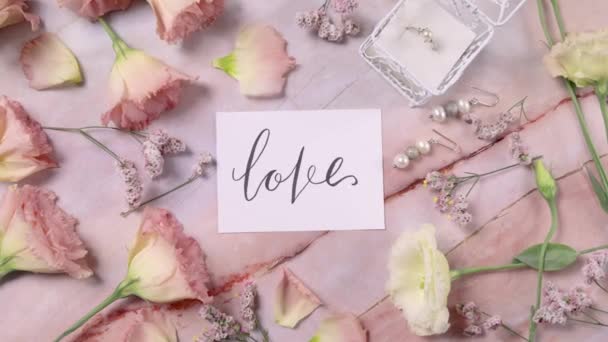 Открытка LOVE на мраморном столе рядом с розовыми цветами  - Кадры, видео