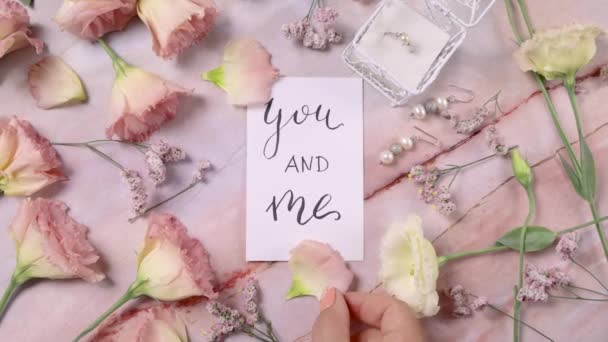 Ty i ja karta na marmurowym stole w pobliżu różowych kwiatów widok z góry zoom  - Materiał filmowy, wideo