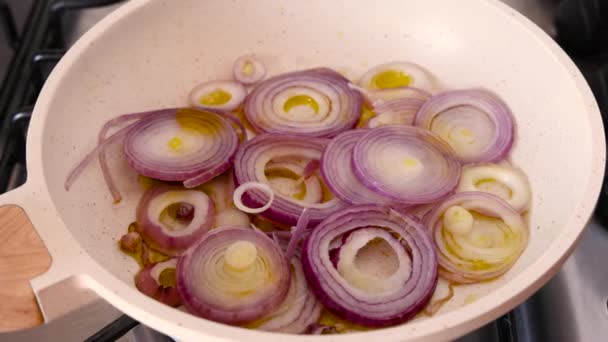 Frying sliced raw purple onions in white frying pan with heated olive oil close up zoom in - Footage, Video