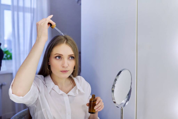 Young woman treating her hair using medical drops. Medicine for care and nutrition of hair, from hair loss. - Foto, Imagem