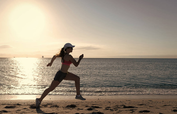 Energetic running woman in activewear run on beach sand along seaside, runner - Photo, Image