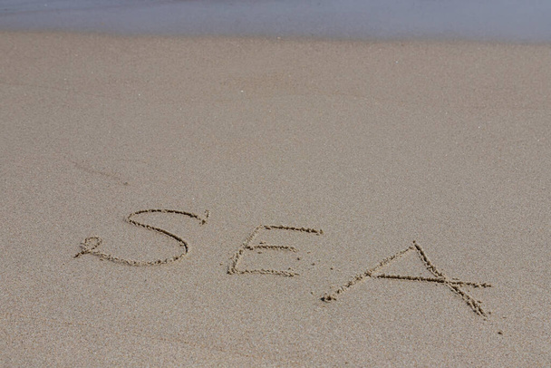 La inscripción mar en la arena por el agua y la ola ascendente, vacaciones en la playa junto al mar. - Foto, imagen
