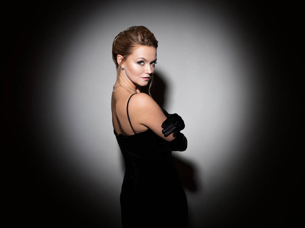 A femme fatale in a black dress with an open back and long velvet gloves. - Фото, изображение