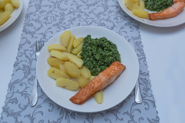 Baked salmon with potatoes and green spinach on a white plate. Delicious food for lunch. - Fotoğraf, Görsel