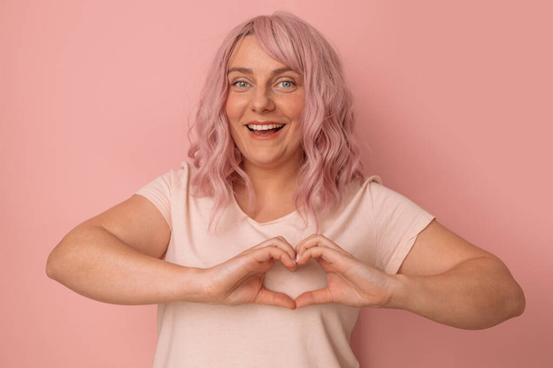 Cute and funny pink hair woman young woman feels happy and romantic making heart shape poses against pink background. - Foto, afbeelding