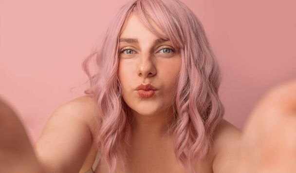Πορτρέτο του αρκετά σέξι κορίτσι με ροζ σγουρά μαλλιά σε εσώρουχα λήψη selfie φωτογραφία θέτοντας απομονωμένη σε ροζ φόντο - Φωτογραφία, εικόνα