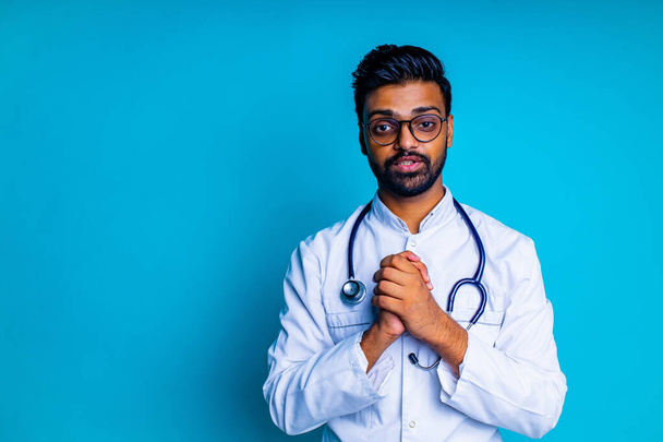 young latin hispanic medican man wear eye glasses with stethoscope in blue studio wall background - Φωτογραφία, εικόνα