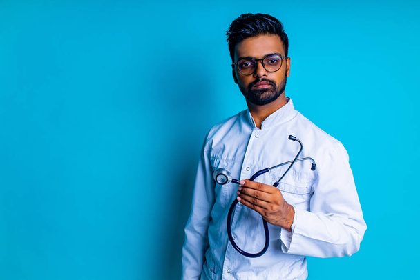 young latin hispanic medican man wear eye glasses with stethoscope in blue studio wall background - Foto, afbeelding