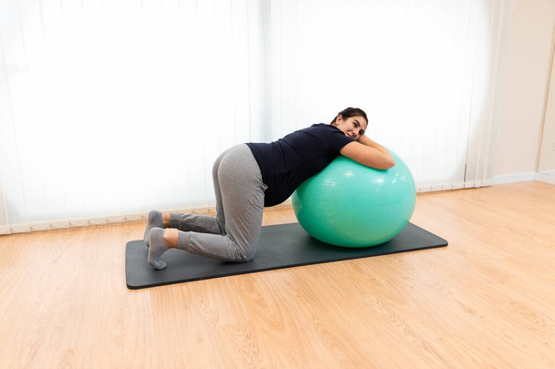Een zwangere vrouw die ademhalingsoefeningen doet en rust op een fitnessbal - Foto, afbeelding