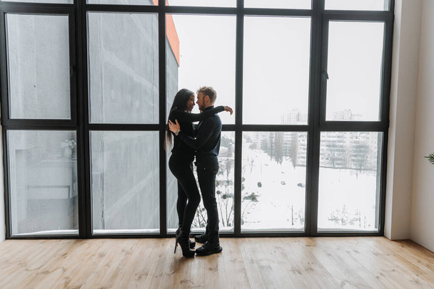 Verliebtes Paar umarmt sich zärtlich in gemütlicher Wohnatmosphäre und Panoramafenster - Foto, Bild
