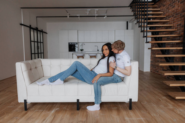 A married couple is sitting on a luxurious white sofa in their new apartment - Фото, изображение