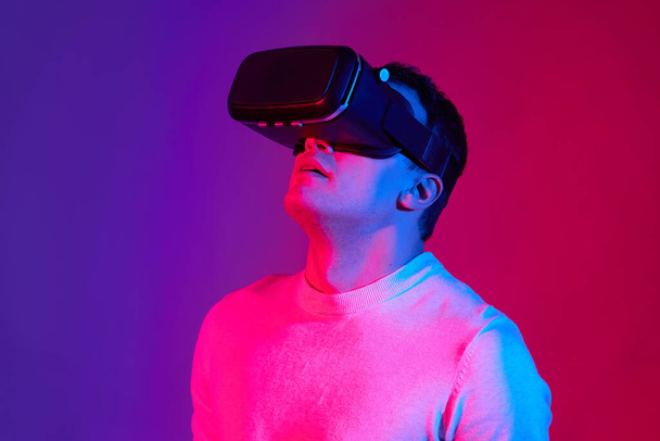 Un jeune homme avec un casque de réalité virtuelle sur la tête sur un fond rouge et bleu. - Photo, image