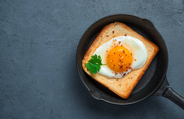 Fried eggs with pepper and parsley on toast in a frying pan on a graphite background. Top view, copy space. - Photo, Image