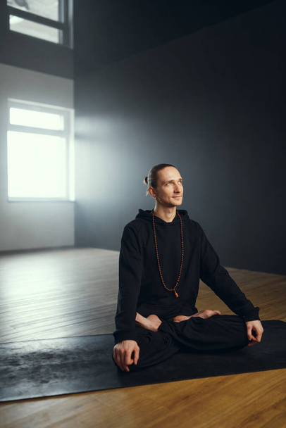 The yogi man sits in the padmasana. Yoga practice in the studio. - Fotografie, Obrázek