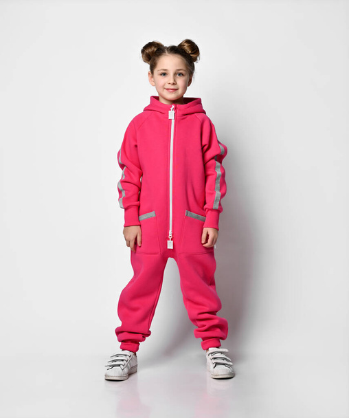 stylish girl in a sports pink suit. little schoolgirl stands in full growth on a white background. hip hop dancers wear stylish cotton tracksuit, hooded pajamas, fashion design for kids - Foto, Imagen