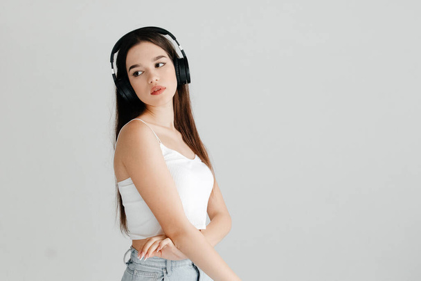 Young woman wearing casual clothes - white top and jeans, black headphones, listening to - Фото, изображение