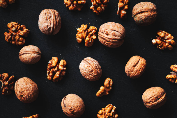 Whole and peeled walnuts on a black background. Close-up, flat lay, top view. Food background, selective focus.  - Photo, Image