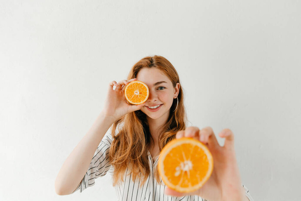 Gülen çekici kız elinde turuncu kesikle beyaza sarılmış. Kış için mükemmel bir meyve. - Fotoğraf, Görsel