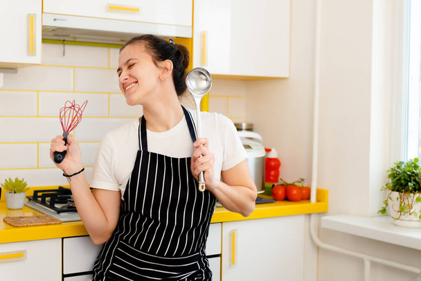 giovane casalinga tiene un mestolo e una frusta e si è divertita in cucina - Foto, immagini