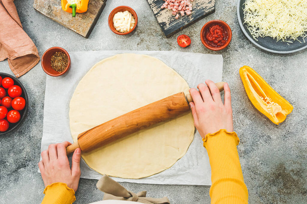 Mains d'un adolescent caucasien dans un tablier dérouler la pâte à pizza avec un rouleau à pâtisserie. - Photo, image