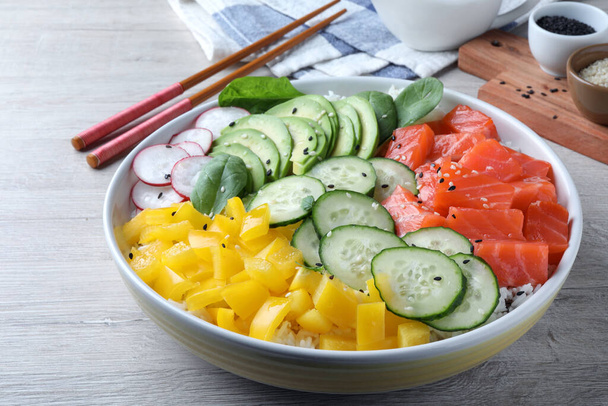 Delicious poke bowl with salmon and vegetables served on wooden table, closeup - Zdjęcie, obraz