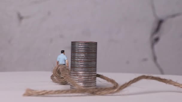 Ένας μικροσκοπικός άνδρας υφασμένος με σωρούς νομισμάτων και σχοινιών. Έννοια για τις οικονομικές δυσκολίες. - Πλάνα, βίντεο