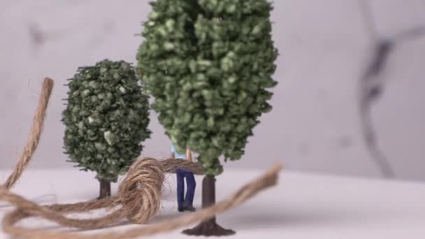 Een miniatuurman vastgebonden aan een miniatuurboom en touw. Begrip geslacht en vooroordelen in de samenleving. - Video
