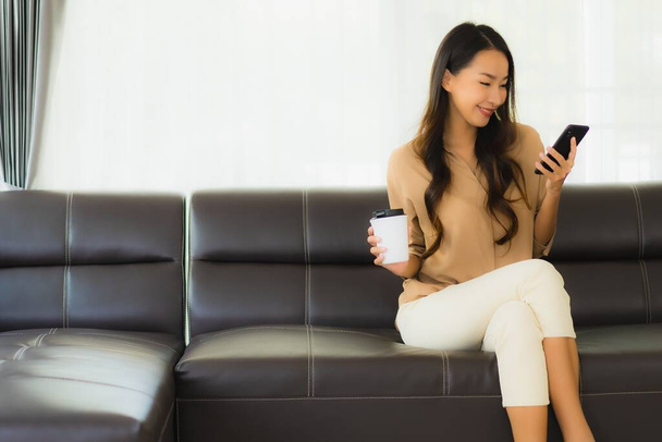 Ritratto bella giovane donna asiatica utilizzare smartphone cellulare o cellulare con tazza di caffè sul divano soggiorno interno
 - Foto, immagini