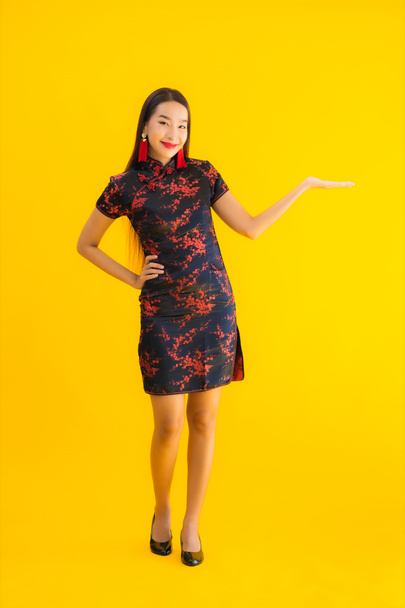 Porträt schöne junge asiatische Frau tragen chinesisches Kleid mit Aktion für chinesisches Neujahrskonzept auf gelbem Hintergrund - Foto, Bild