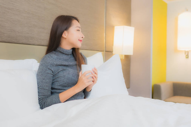Portret piękna młoda azjatycka kobieta z filiżanką kawy na łóżku we wnętrzu sypialni - Zdjęcie, obraz