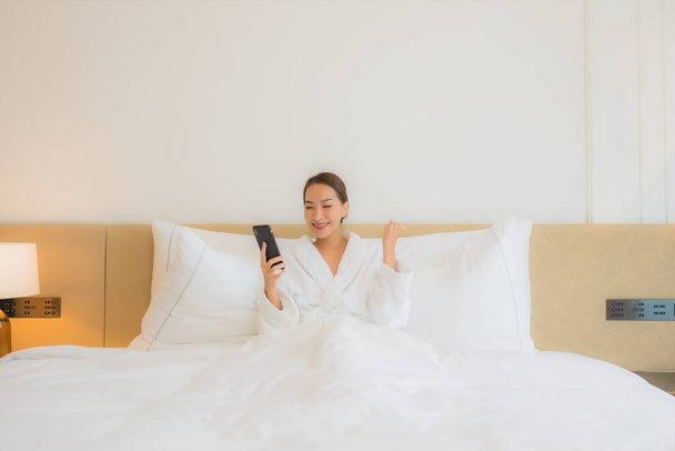 Πορτρέτο όμορφη νεαρή ασιατική γυναίκα χρησιμοποιούν έξυπνο κινητό τηλέφωνο στο κρεβάτι στο εσωτερικό του υπνοδωματίου - Φωτογραφία, εικόνα