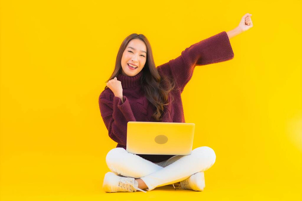 Porträt schöne junge asiatische Frau verwenden Computer-Laptop auf gelbem Hintergrund isoliert - Foto, Bild