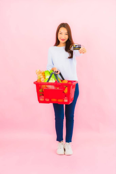 Portrait beautiful young asian woman with fruit vegetable and grocery in basket on pink isolated background - Photo, Image