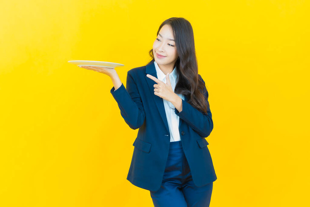Porträt schöne junge asiatische Frau lächeln mit leeren Teller Teller auf farbigem Hintergrund - Foto, Bild