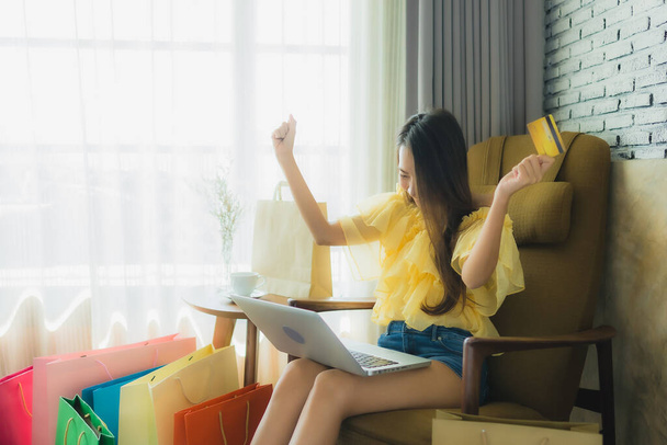 Retrato jovem mulher asiática usando laptop para compras on-line com xícara de café e livro na sala de estar interior
 - Foto, Imagem