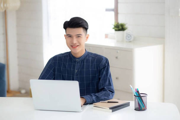 Młody biznesmen pracujący w domu z laptopem na biurku, niezależny mężczyzna siedzi w domu używając notebooka do komunikacji i relaksu na stole, przedsiębiorca w biznesie startującym, nowa normalna. - Zdjęcie, obraz