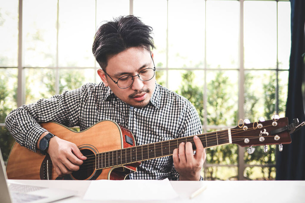Азійський музикант грає на гітарі в студії звукозапису. Грає живу музику Акустика або класичний музичний жанр. Митець Соло. Пісенник. - Фото, зображення