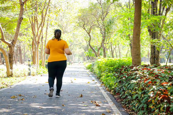 Sarı bluz giyen şişman Asyalı kadın sabah parkta koşuyor. Şişman insanların sağlığı için kilo verme egzersizi kavramı. Boşluğu kopyala - Fotoğraf, Görsel