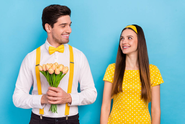 Photo of two peaceful idyllic partners look each other hold yellow tulips isolated on blue color background - Zdjęcie, obraz