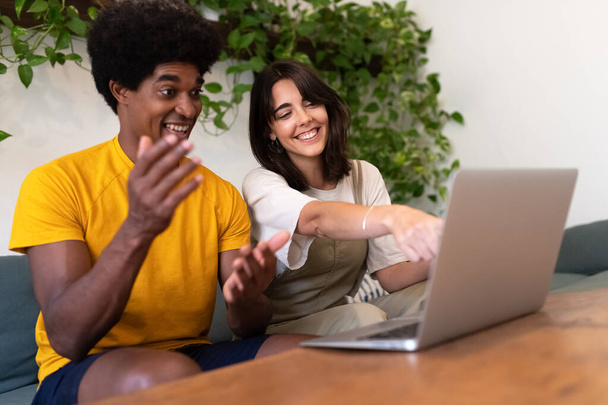 Jeune couple interracial regardant ordinateur portable. Femme pointe l'écran avec le doigt. L'homme a surpris l'expression. - Photo, image