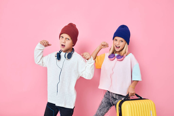 веселый мальчик и девочка желтый чемодан с наушниками студия позирует - Фото, изображение