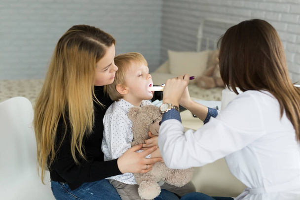 Doctor examine childs throat. Boy and mother at pediatrician office - Фото, зображення