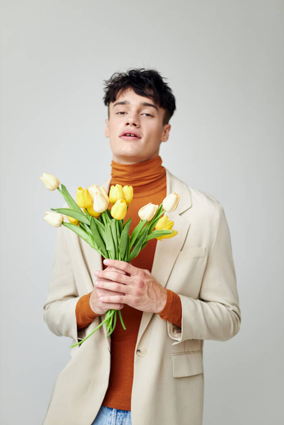 pretty man in white jacket with a bouquet of yellow flowers elegant style model studio - Foto, imagen