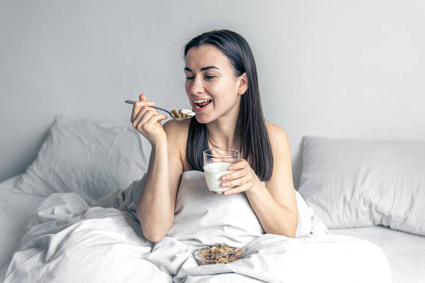Eine junge Frau im weißen Bett mit Müsli und Milch. - Foto, Bild