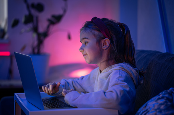 A little girl uses a laptop late at night. - Foto, afbeelding