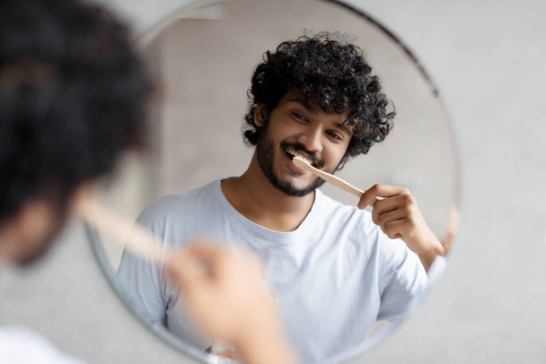 Toothcare routine concept. Young indian guy cleaning teeth in the morning using toothbrush and toothpaste - Foto, afbeelding